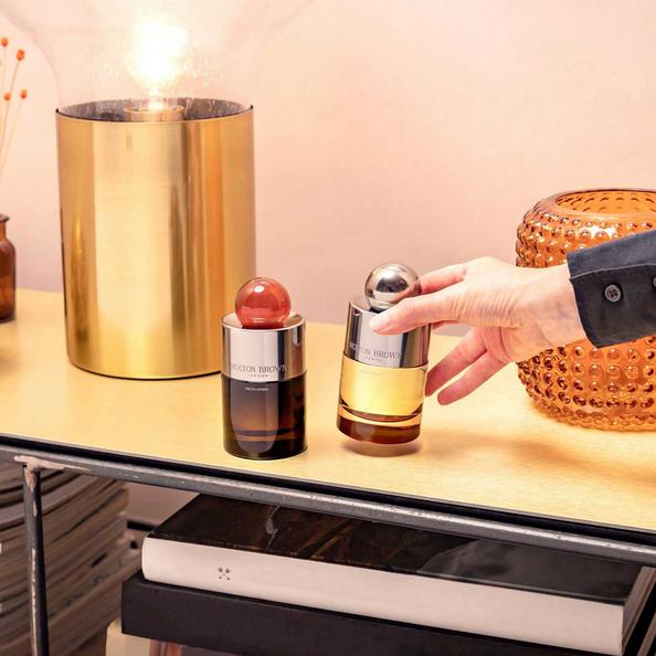 An image of Molton Brown Eau De Parfum and a hand lifting a Bottle of Eau De Toilette