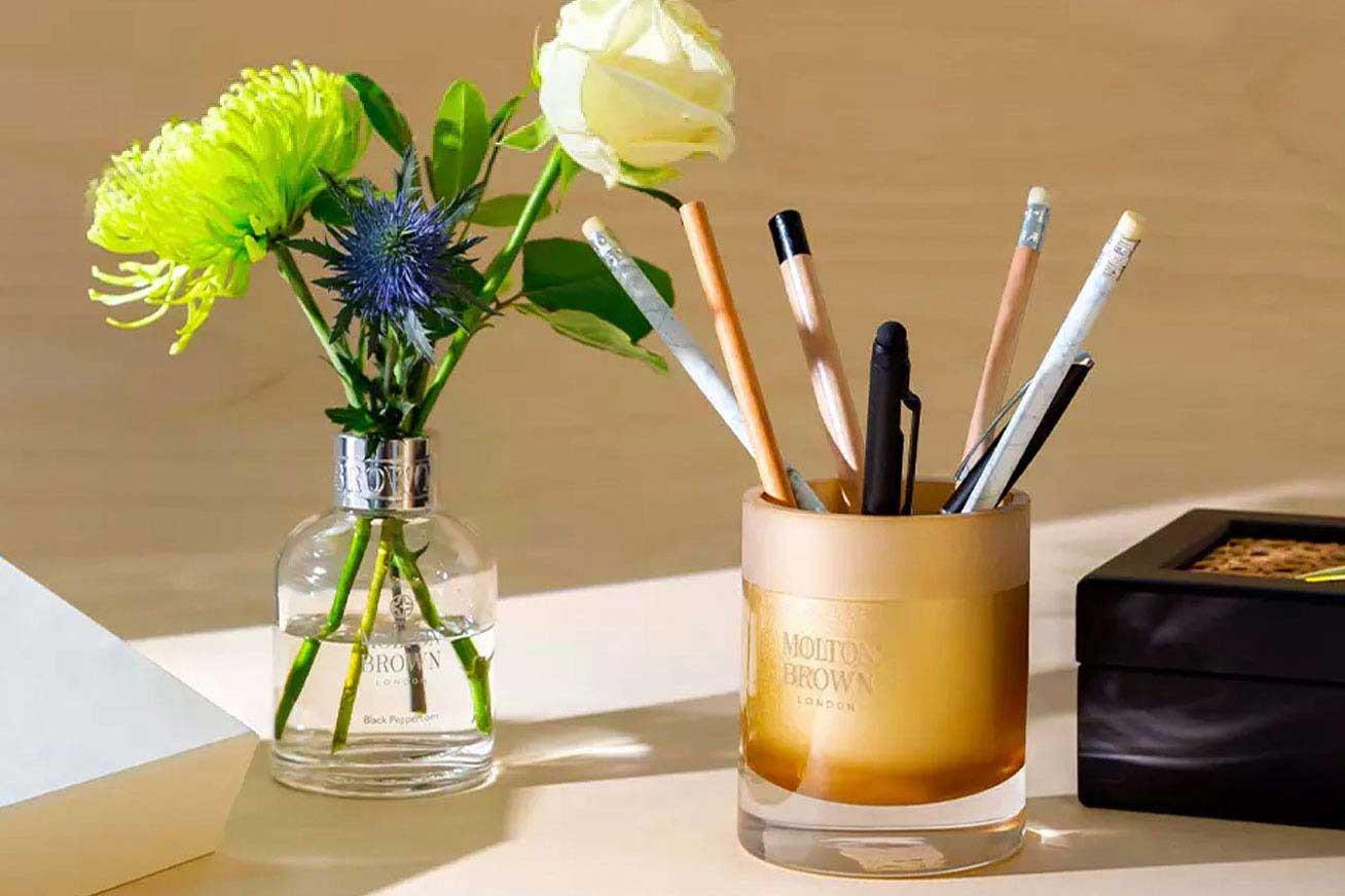Image of a Molton Brown Aroma Reed bottle being used as a vase, and a Molton Brown candle being used as a pen holder