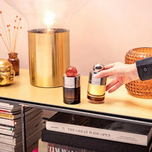 An image of a Molton Brown bottle of Eau de Parfum and Eau de Toilette and a hand lifting one of the bottles